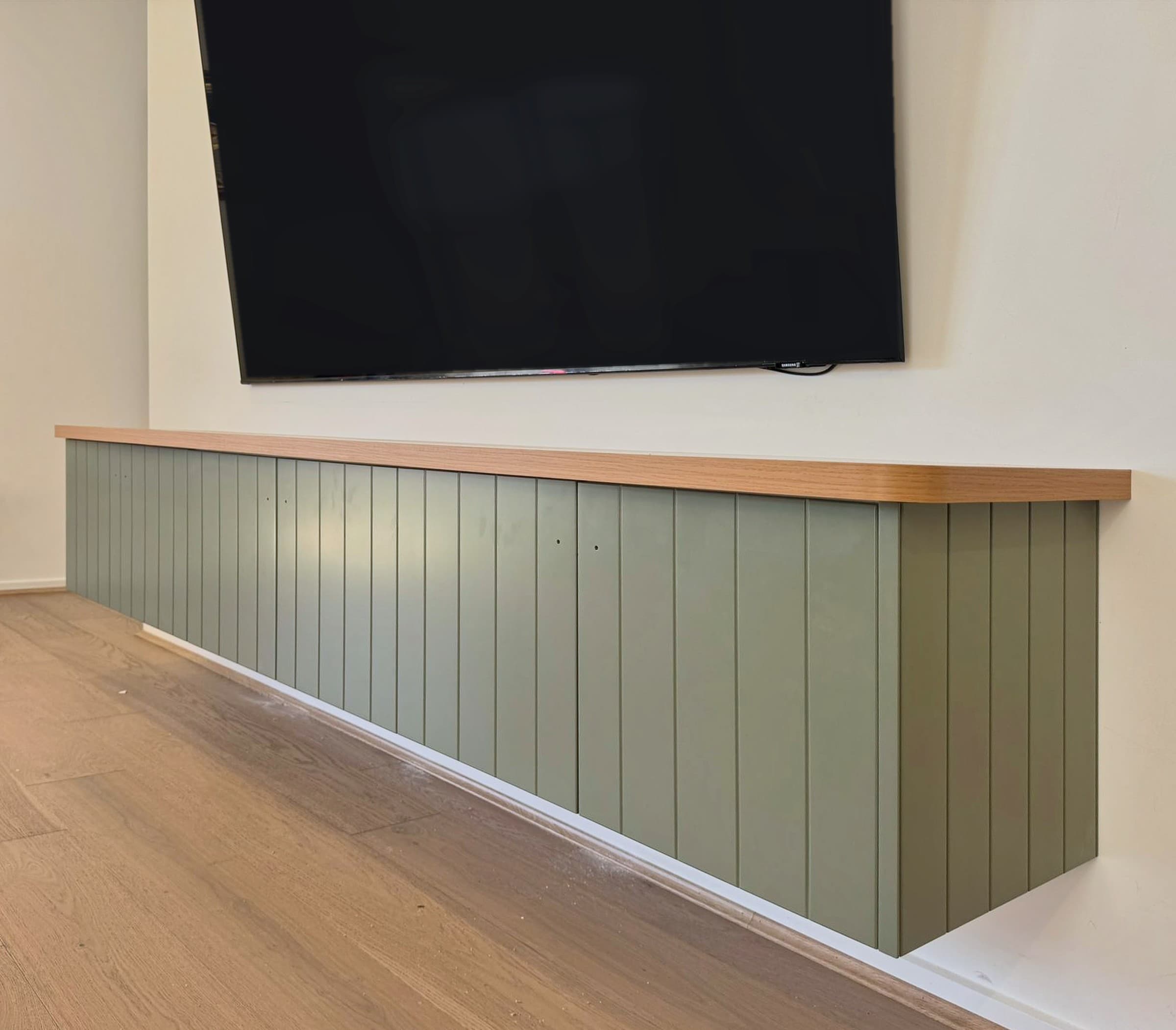 Floating TV unit in sage green V-groove panelling with a solid timber-look top.