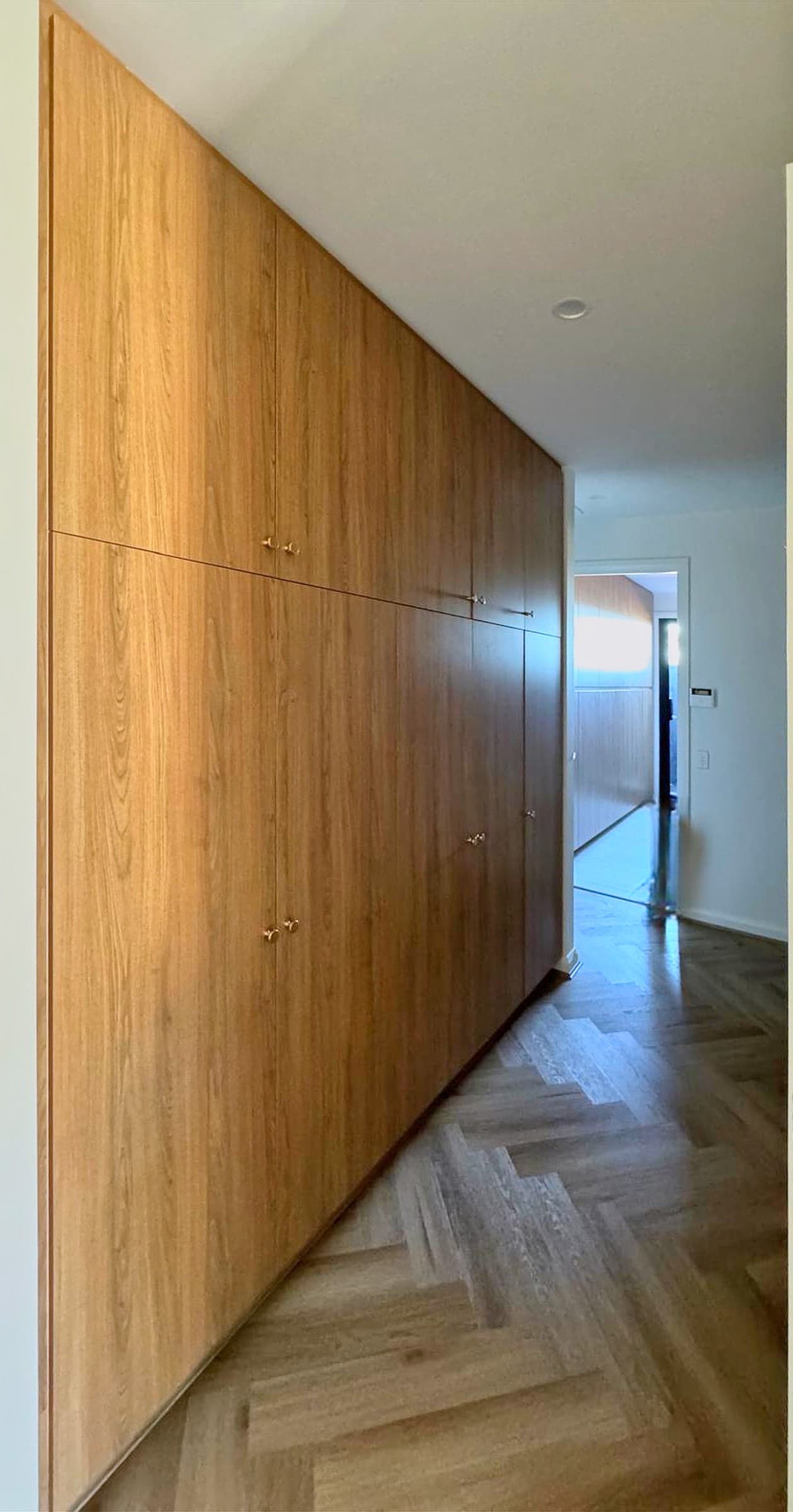 Hallway wall of full-height timber-grain robes with brass knobs, built flush along the corridor.